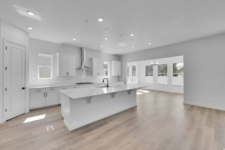 Bright kitchen featuring white cabinetry, a large center island with a stone-finish countertop, a subway tile backsplash, and wood-finish flooring