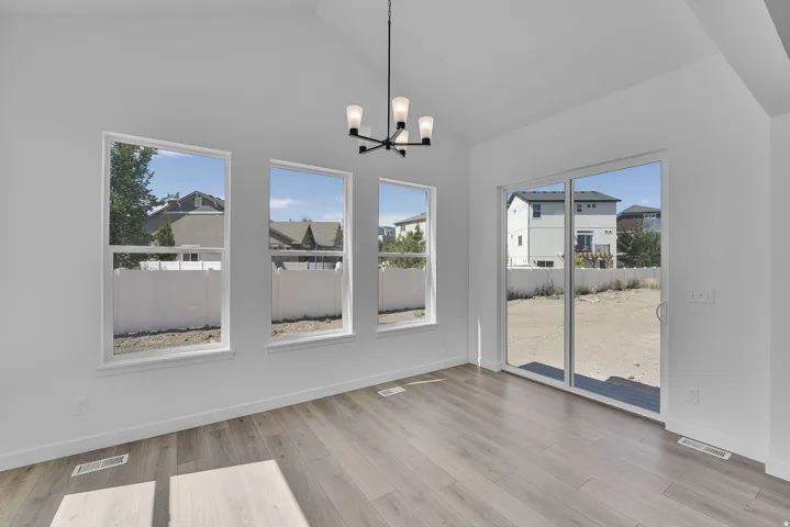 Spacious room featuring vaulted ceilings, three large windows, light wood-finish flooring, a contemporary chandelier, and direct outdoor access via a sliding glass door