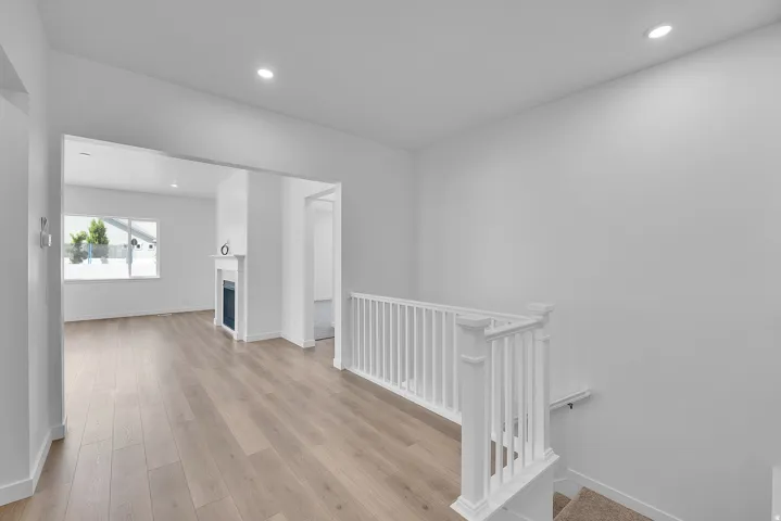Bright interior featuring wood-finish flooring, a white staircase with a classic balustrade, and recessed lighting