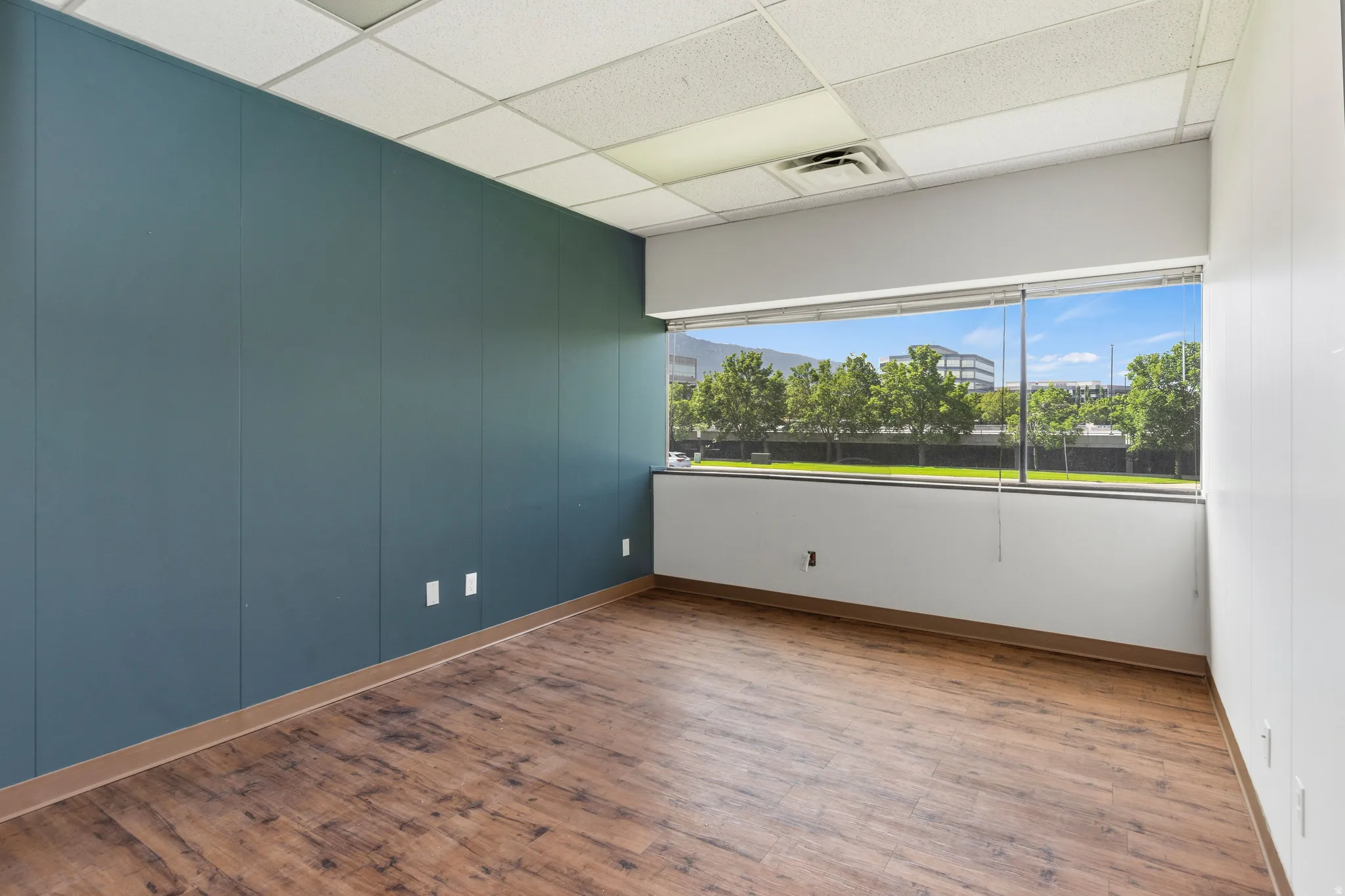 Room featuring wood-finish flooring, a full wall of floor-to-ceiling windows, and a dropped acoustic ceiling