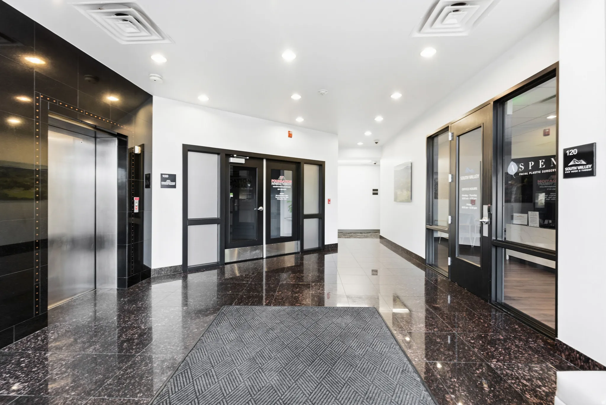 Lobby featuring polished dark granite flooring, recessed lighting, and a stainless steel elevator