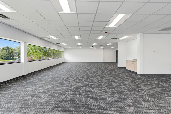 Expansive open-concept room featuring patterned carpet, a drop ceiling with integrated lighting, and a continuous band of windows