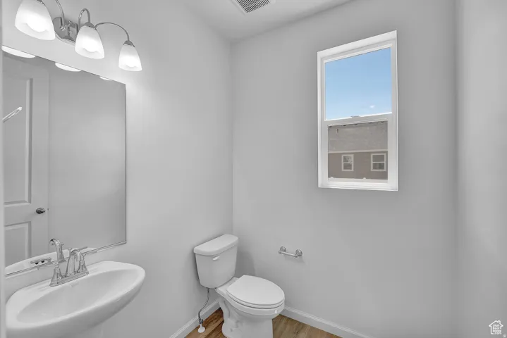 Bright powder room featuring a pedestal sink with chrome faucet, a rectangular wall mirror, and a three-light vanity fixture