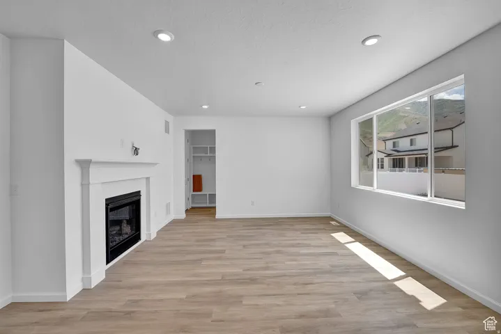 Spacious room featuring wood-finish flooring, a white mantel fireplace, recessed lighting, and a large window