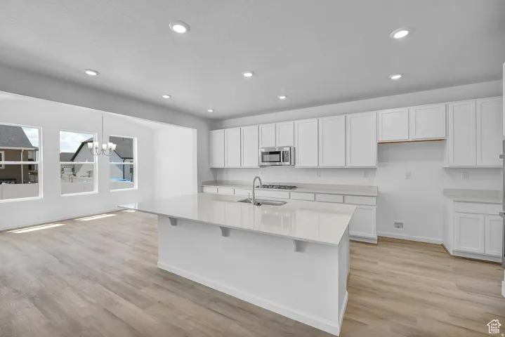Spacious kitchen featuring an extended island with a sink, stainless steel appliances, white cabinetry, recessed lighting, and wood-finish flooring