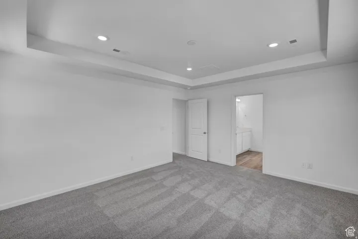 Spacious room featuring tray ceiling with recessed lighting, light gray carpeting, and white trim