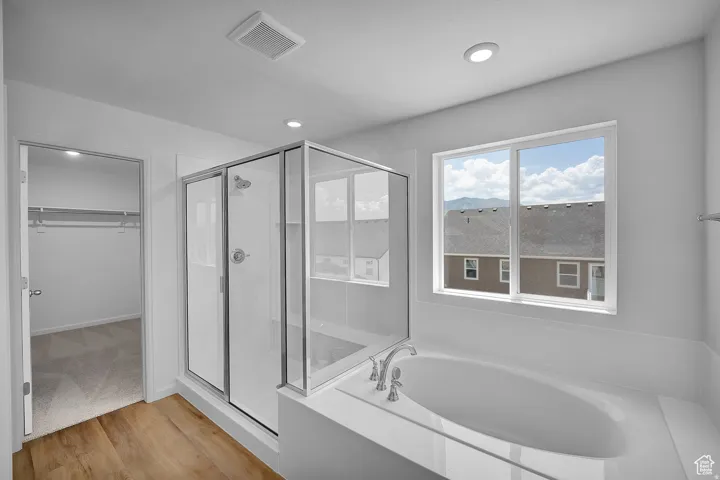 Bathroom featuring a built-in soaking tub, glass-enclosed shower, wood-finish flooring, and a large window