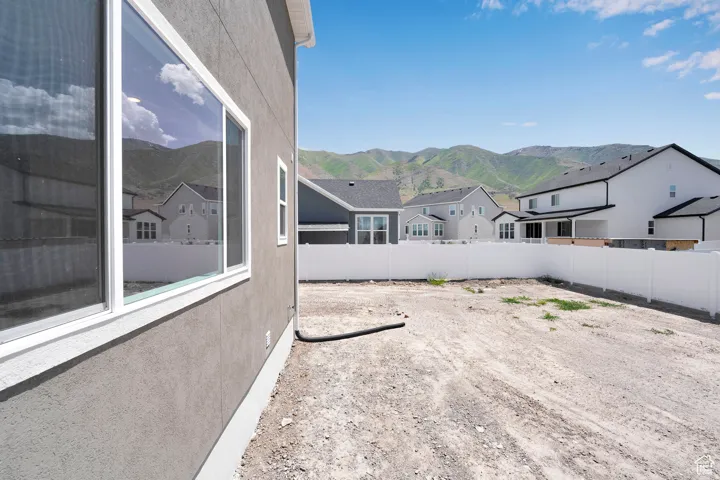 Spacious side yard featuring a stucco exterior with white trim, a large picture window, a white vinyl privacy fence, and mountain scenery