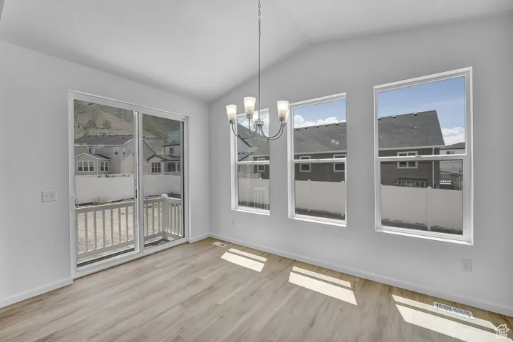 Vaulted ceiling with a contemporary chandelier, light wood-finish flooring, and multiple windows