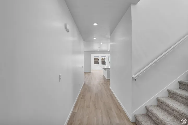Bright hallway featuring wood-finish flooring, recessed lighting, and a carpeted staircase with a white handrail