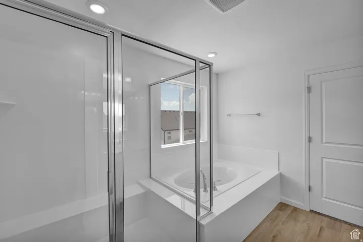 Bathroom featuring a glass-enclosed shower, built-in soaking tub with white tile surround, recessed lighting, and wood-finish flooring