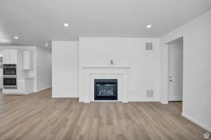 Spacious room featuring a fireplace with a white mantel, recessed lighting, and wood-finish flooring