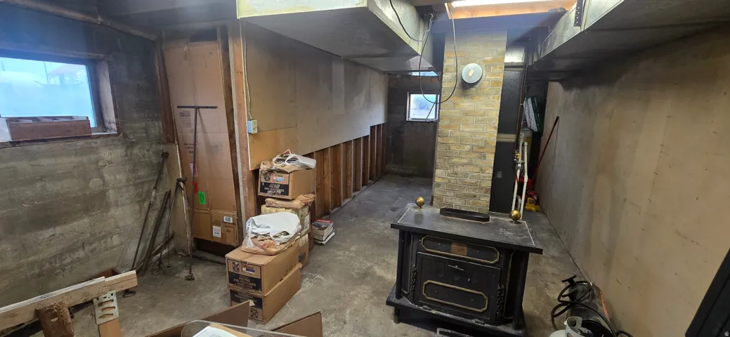 Basement area featuring concrete flooring, a brick chimney, and a wood-burning stove