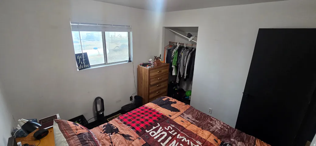 Room featuring a single window with blinds, a built-in closet with hanging rod, and a black interior door