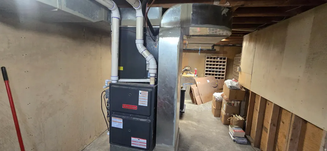 Utility area featuring a furnace system with PVC piping and metal ductwork