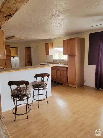 Kitchen featuring wood-finish flooring, wood cabinetry, a light-colored countertop, and a window above the sink