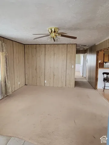 Spacious room featuring paneled walls, a textured ceiling, and a ceiling fan with integrated lighting
