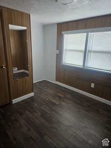 Interior space featuring dark wood-finish flooring, half-paneled walls, a window with blinds, and a built-in mirror