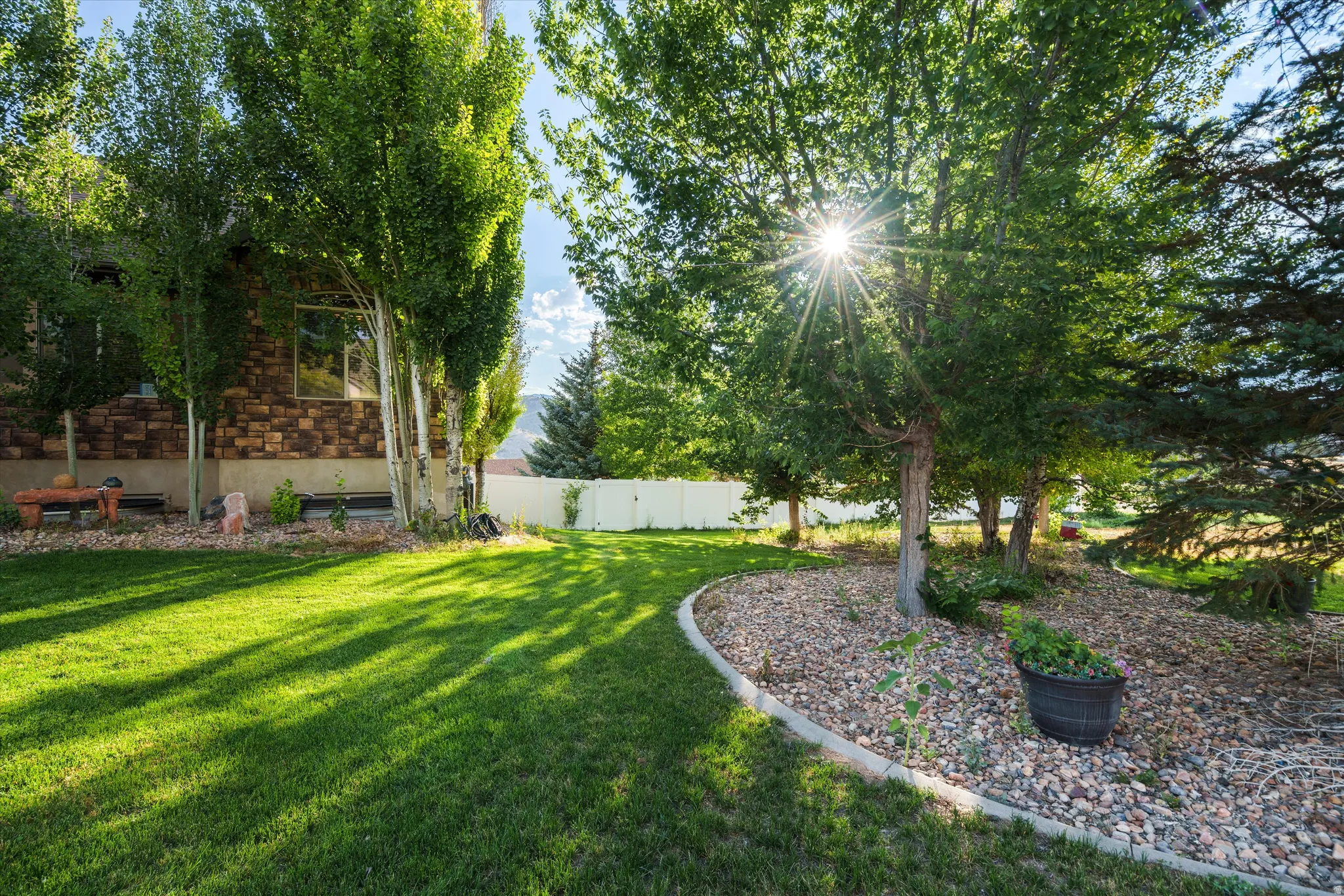 Expansive lawn with mature trees, a defined rock border, and a privacy fence