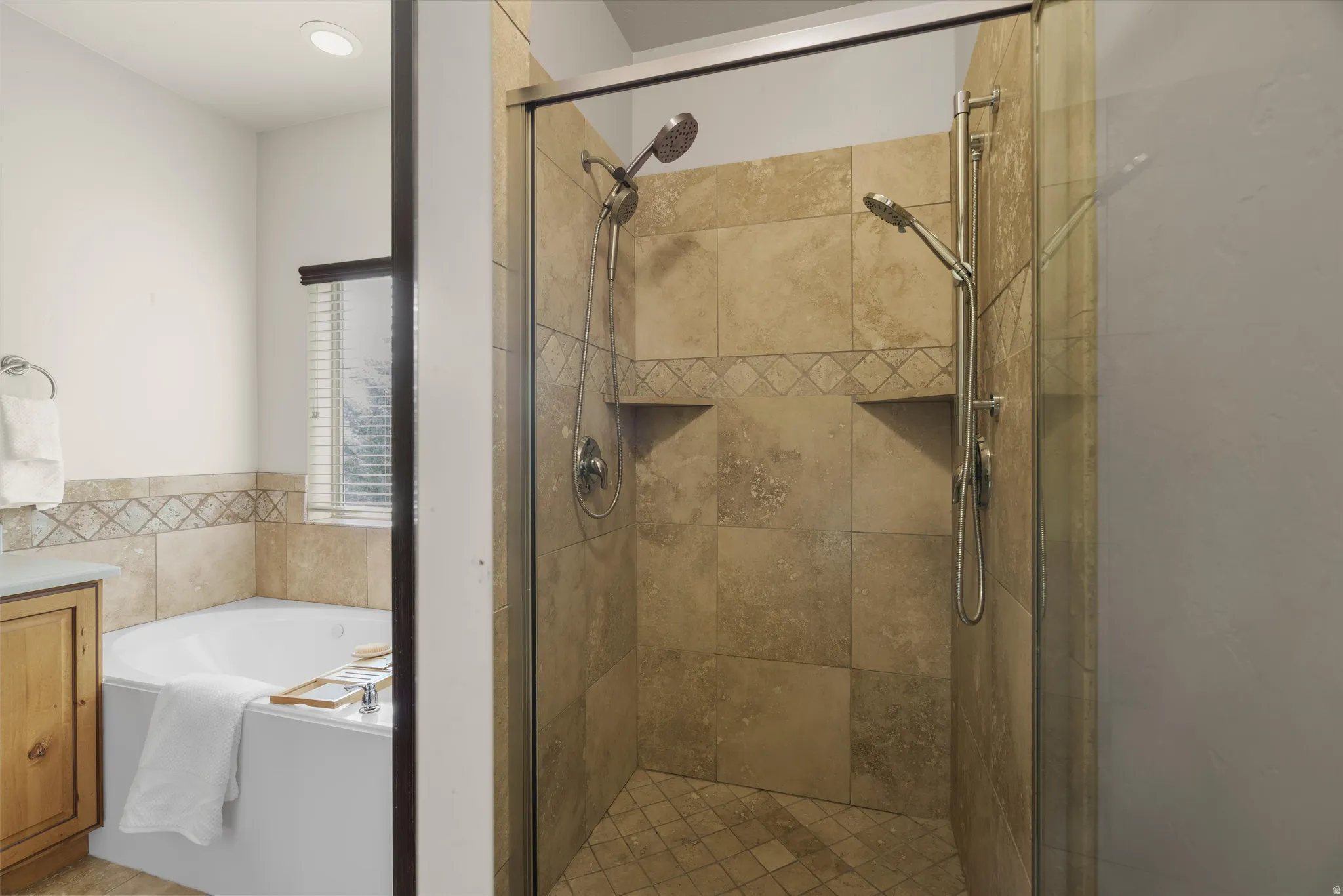 Glass-enclosed shower featuring natural stone tile, dual shower heads, and integrated shelving