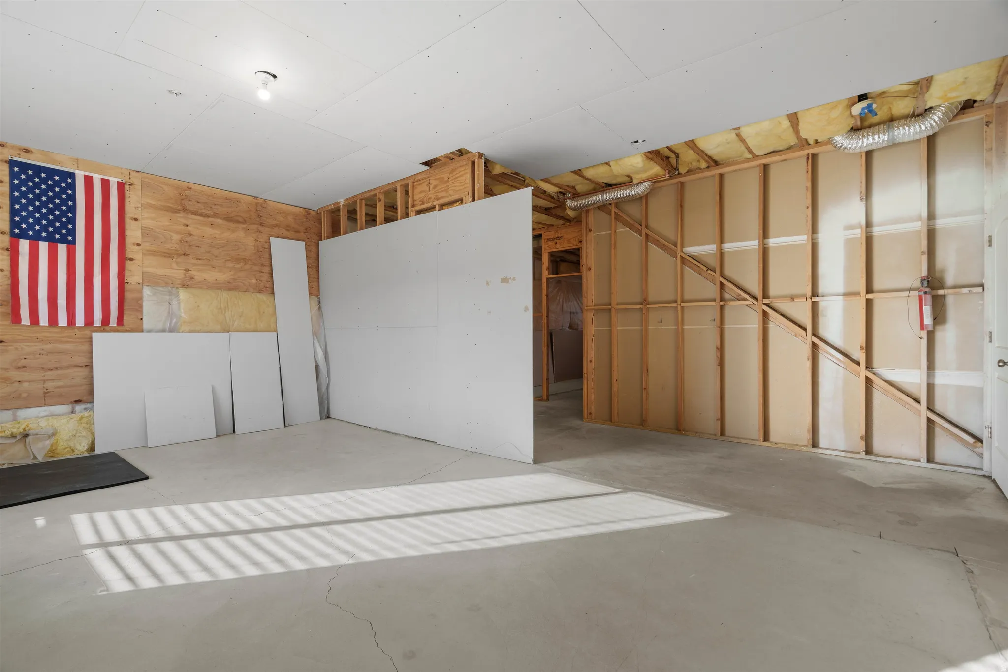 Unfinished interior space featuring exposed wood framing, concrete flooring, drywall sheets, and a ceiling-mounted light fixture