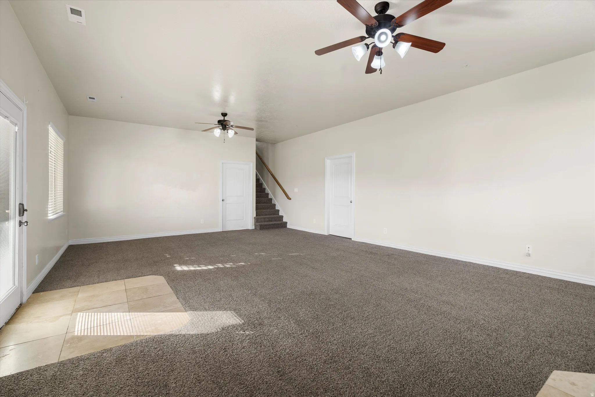 Spacious room featuring neutral carpeting, a tiled entry area, and two ceiling fans with integrated lighting