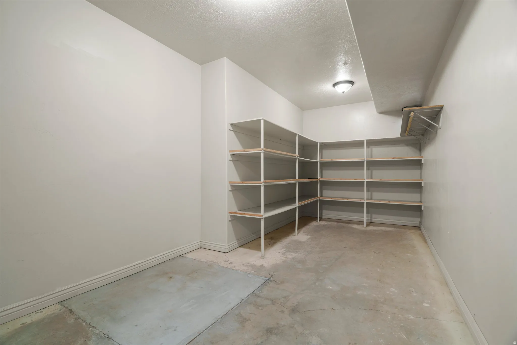 Spacious storage room featuring extensive built-in shelving, concrete flooring, and a ceiling-mounted light fixture