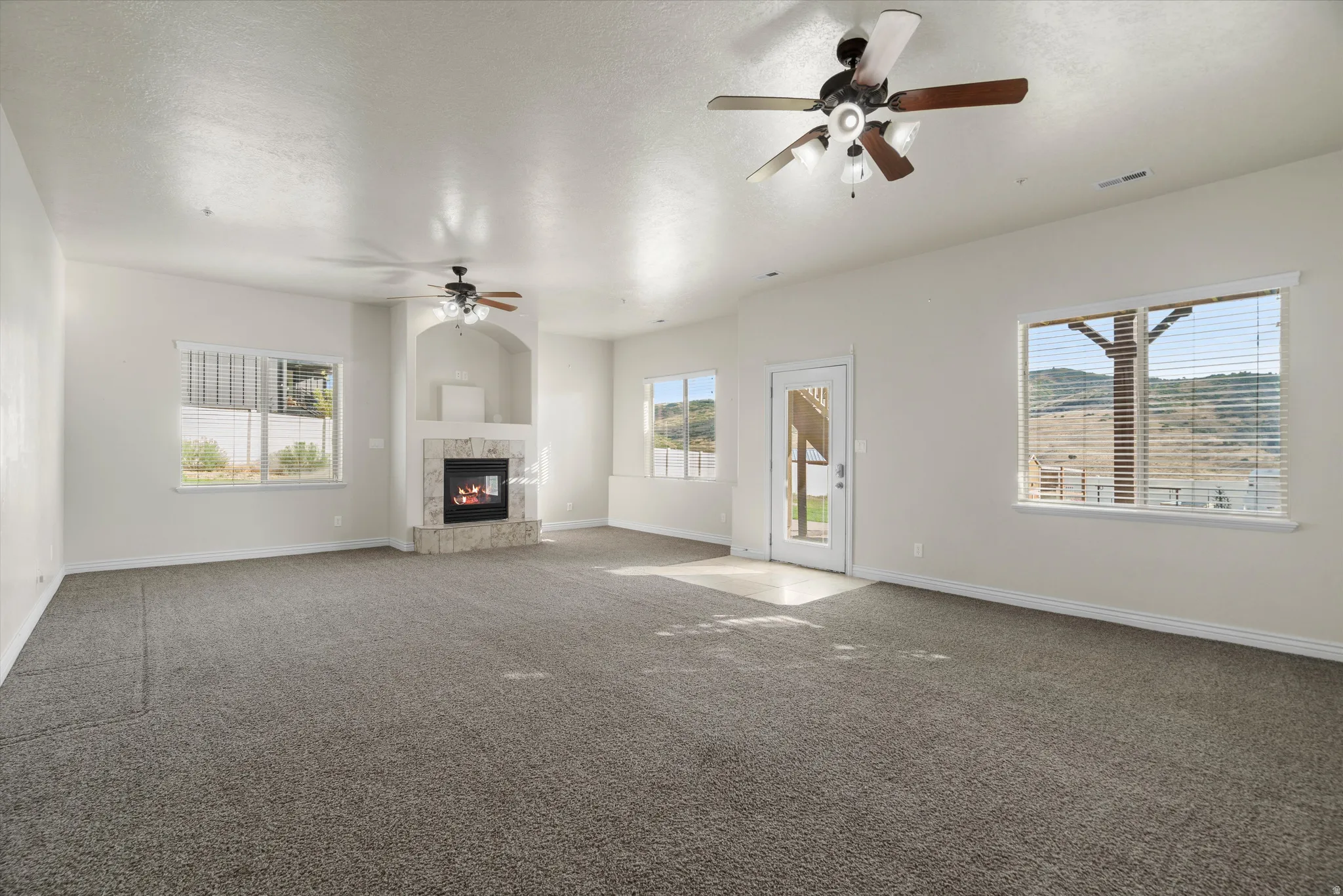 Spacious interior room featuring light-toned walls, textured gray carpeting, and multiple windows
