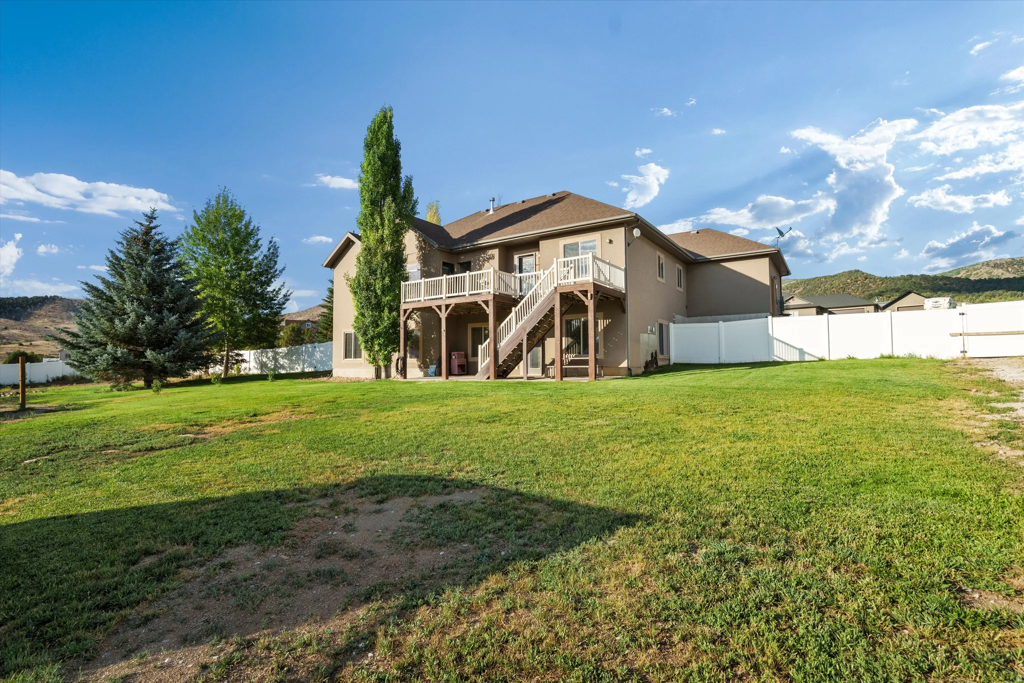 Expansive rear yard featuring a large lawn area, mature trees, and a white privacy fence