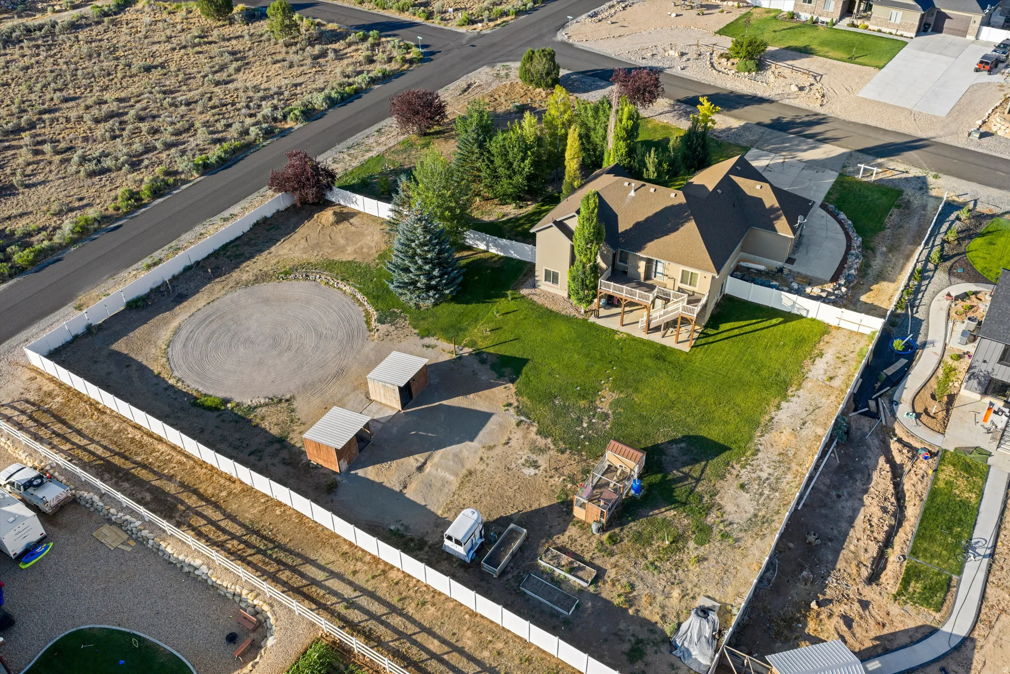 Expansive property featuring a vinyl privacy fence, a circular gravel area, two outbuildings, a multi-level deck, and a manicured lawn