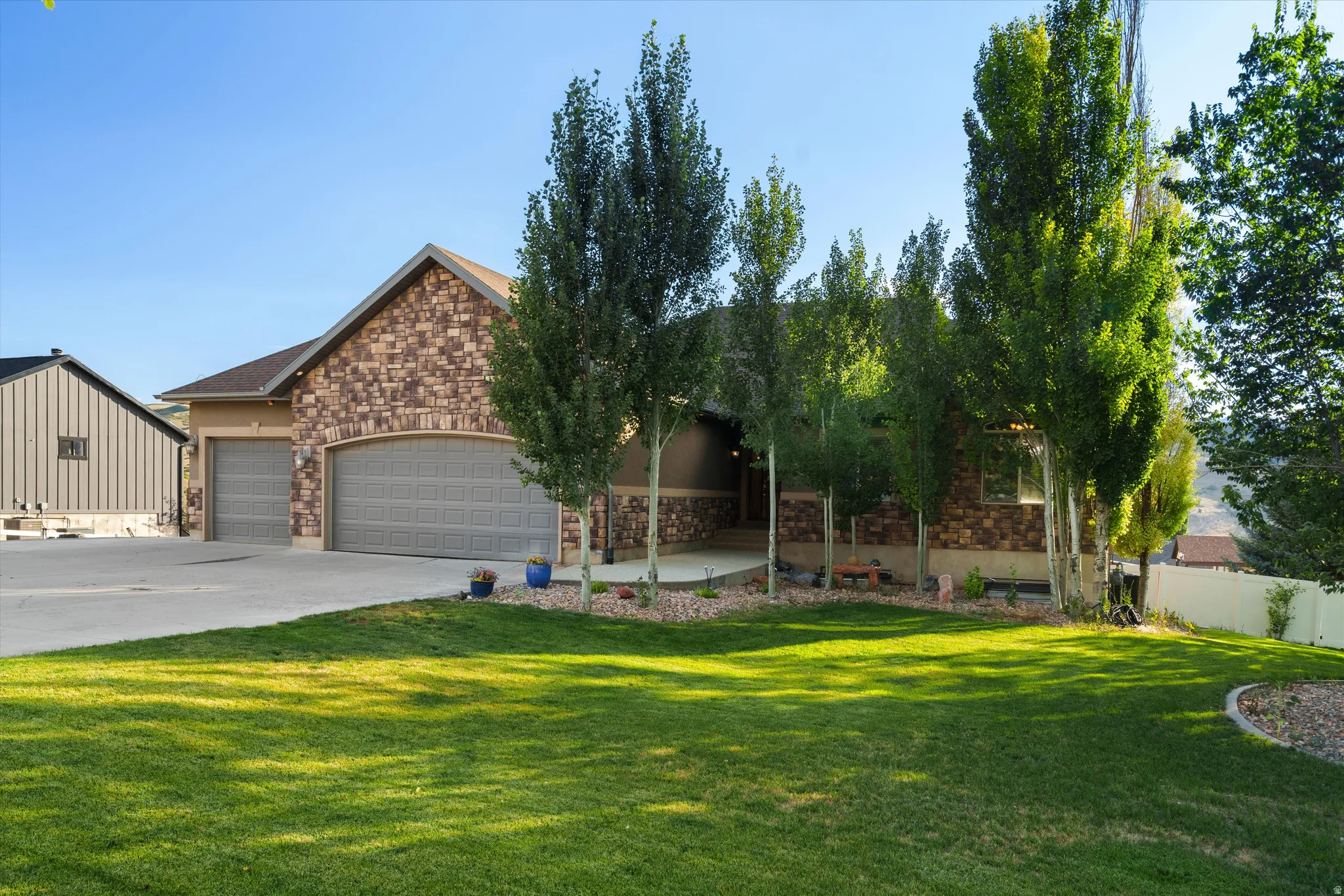 Stone facade residence featuring an attached three-car garage with arched entry, a concrete driveway, and mature landscaping