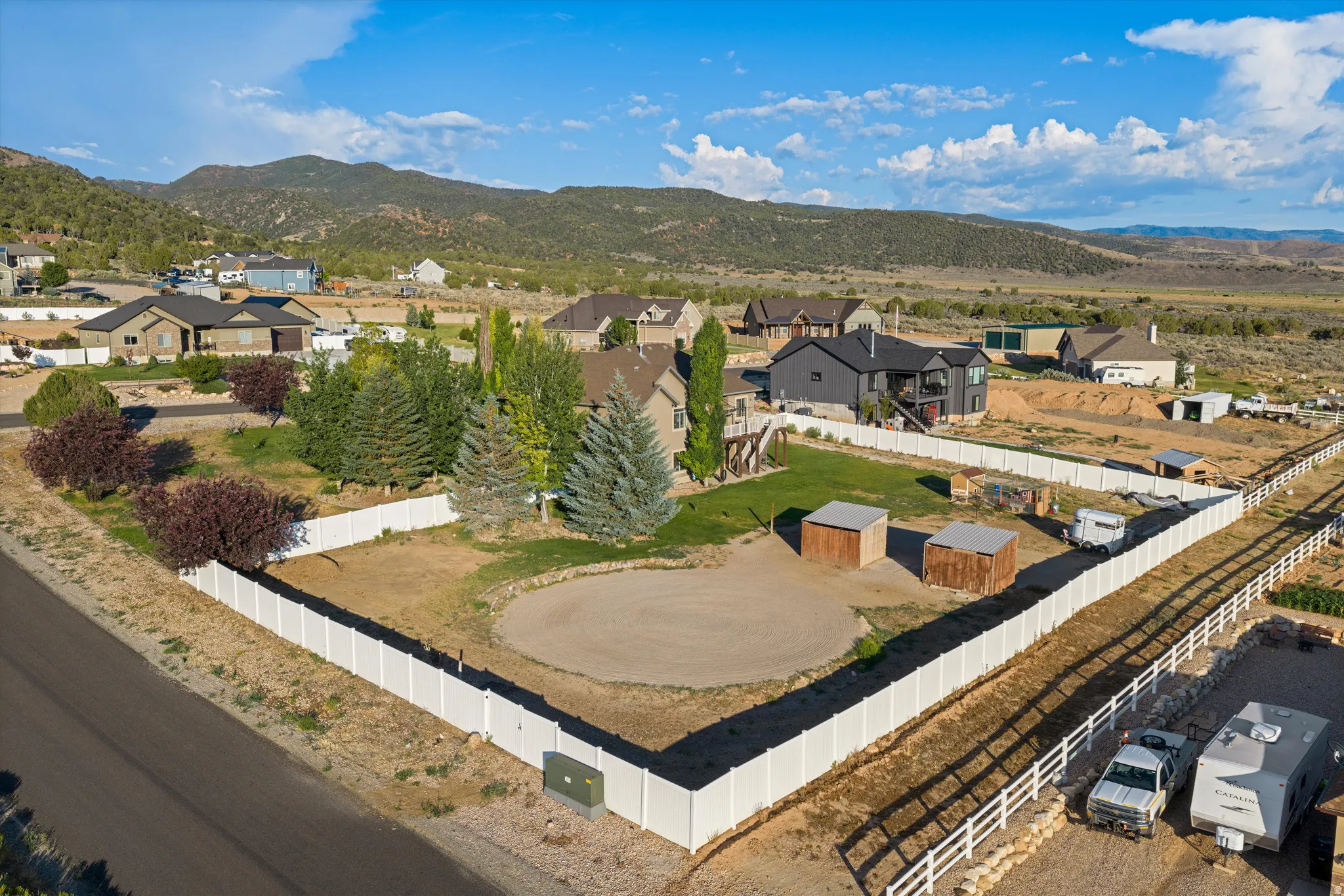 Expansive property featuring a white vinyl perimeter fence, multiple mature trees, and a graded circular area