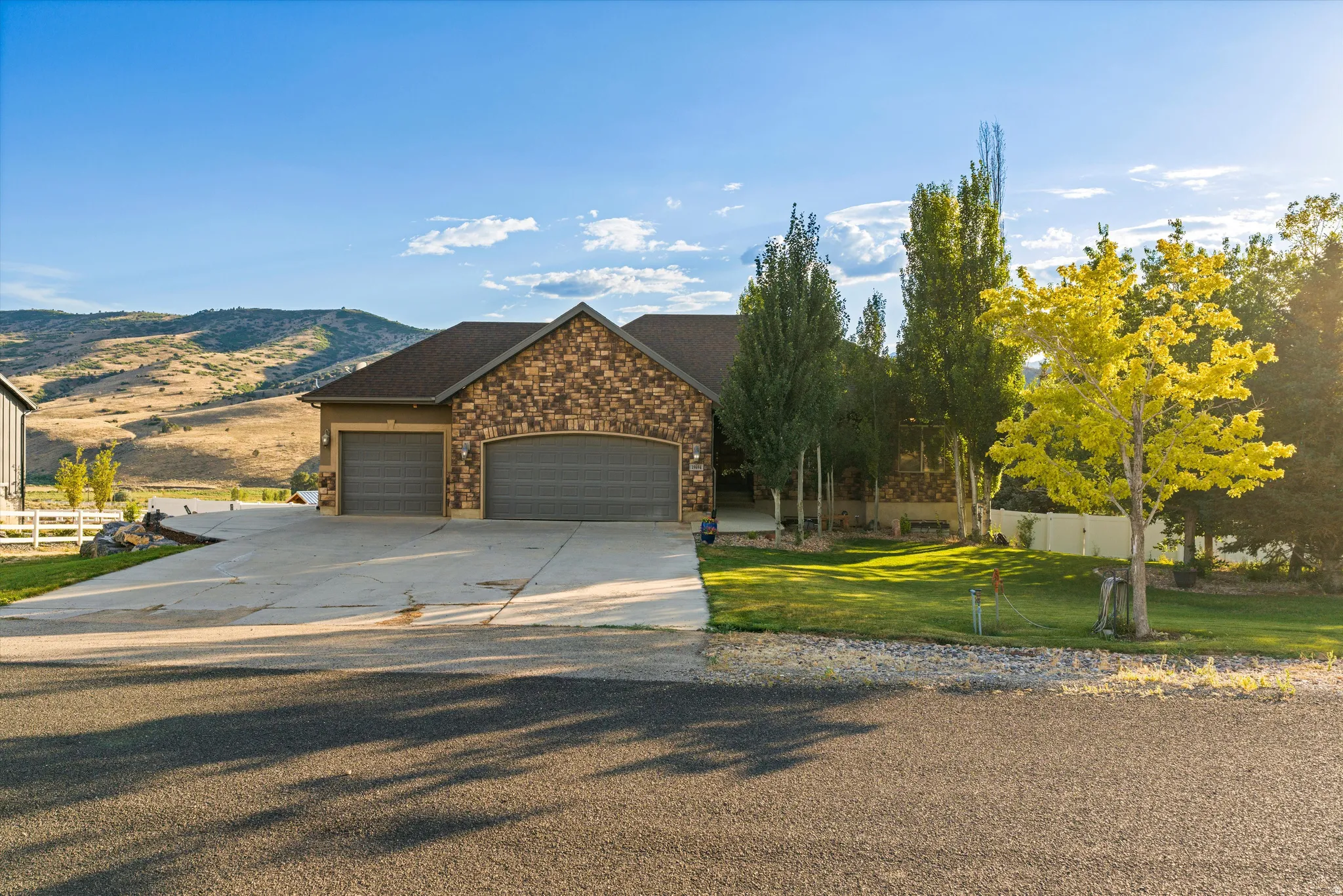 Stone and stucco exterior featuring a dark shingle roof, arched garage doors, and a concrete driveway
