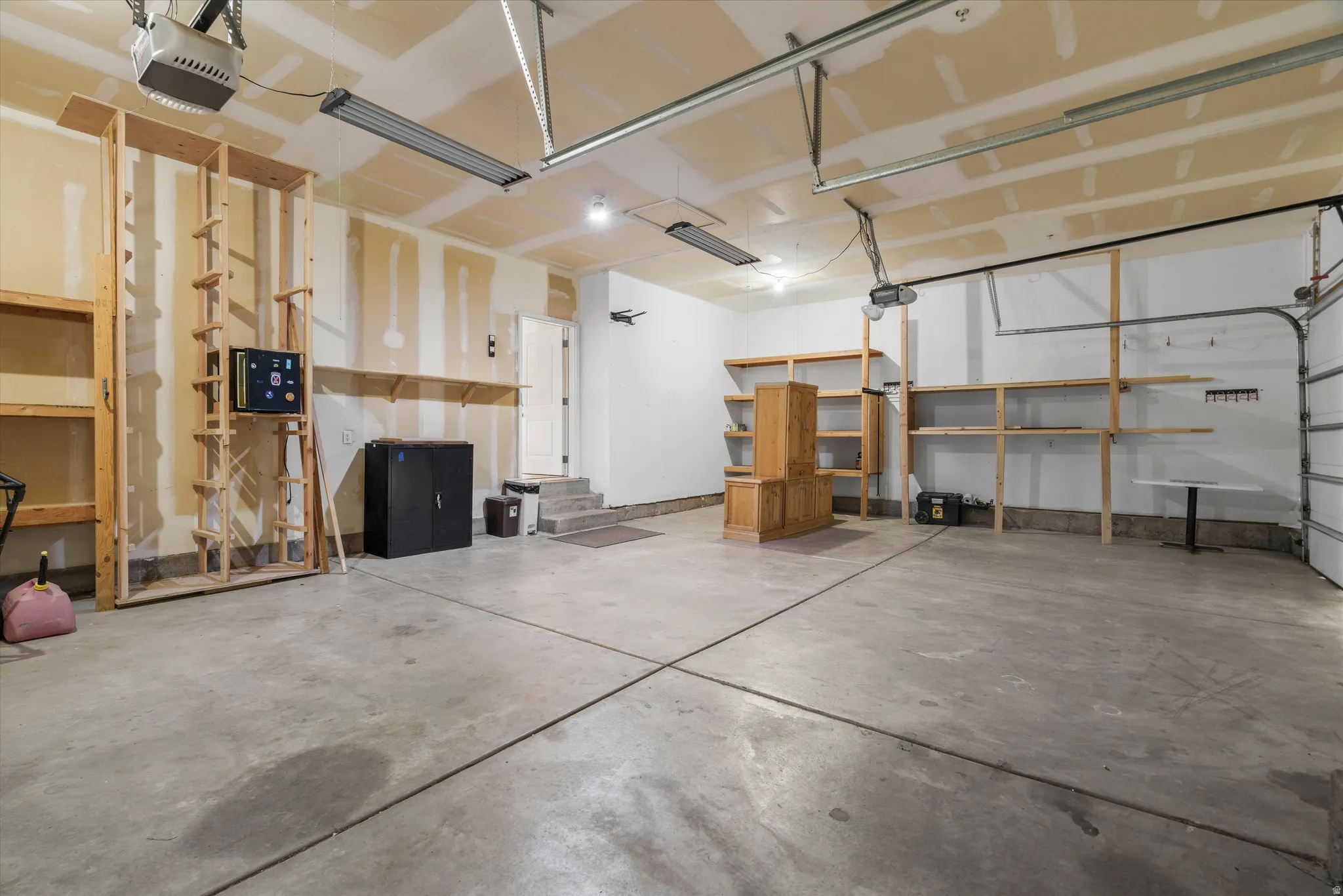 Spacious garage featuring a concrete floor, overhead lighting, garage door opener mechanisms, and extensive built-in wooden shelving units for organization