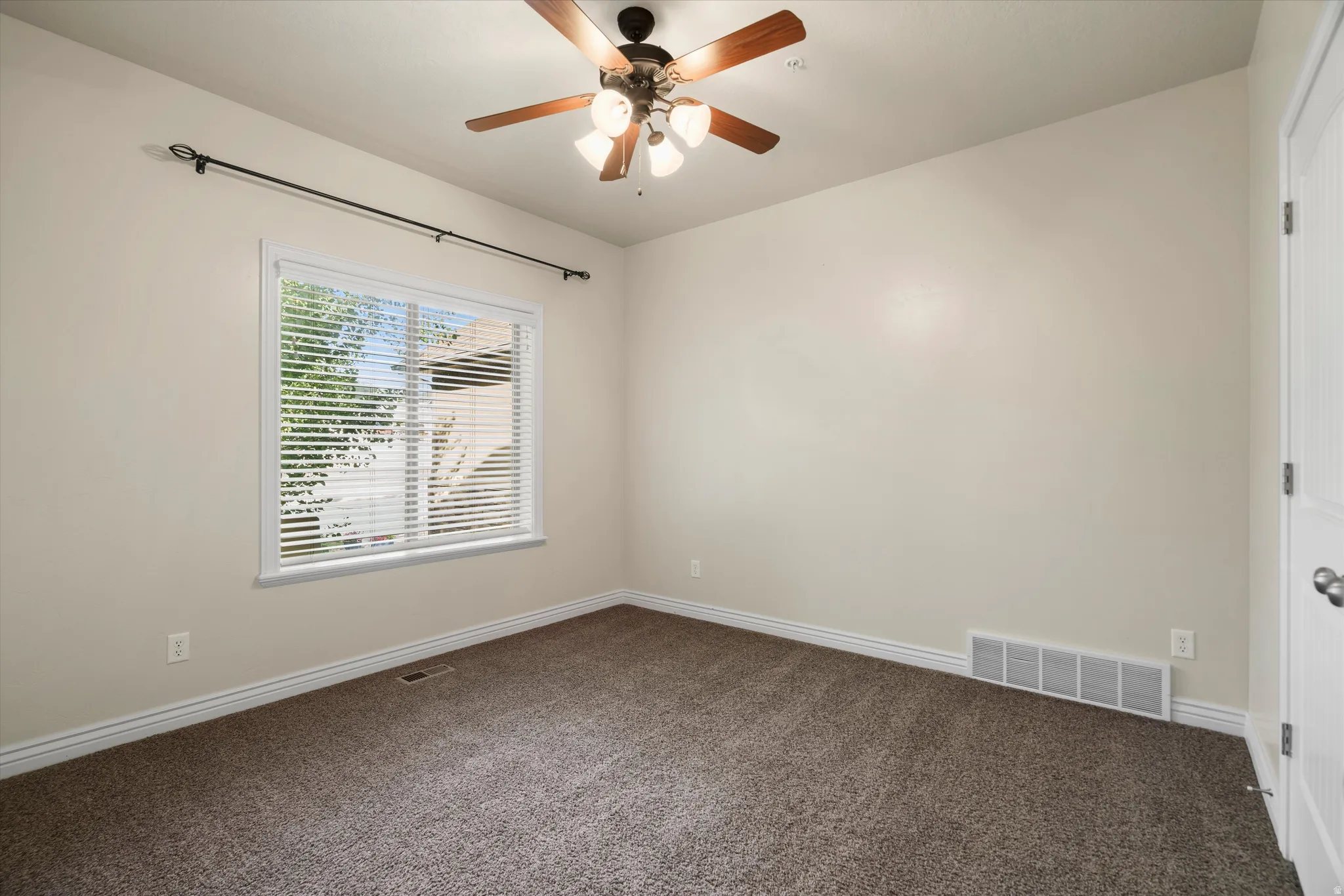Carpeted room featuring a ceiling fan with light fixture, a window with horizontal blinds, and a white paneled door