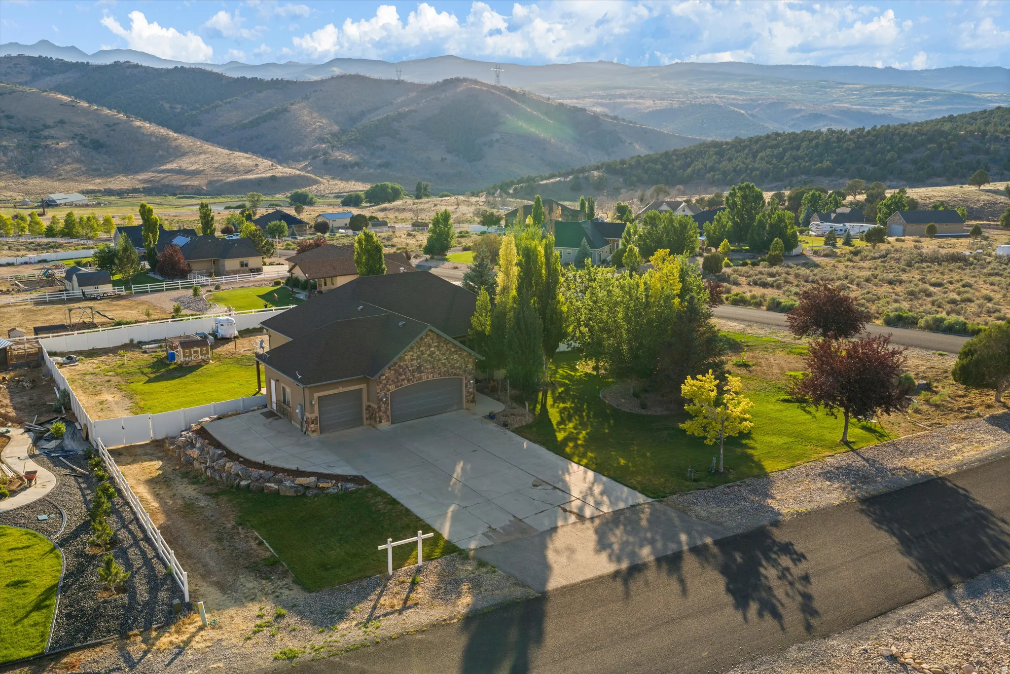 Stone and stucco exterior residence featuring a multi-car garage, concrete driveway, and landscaped front yard with mature trees