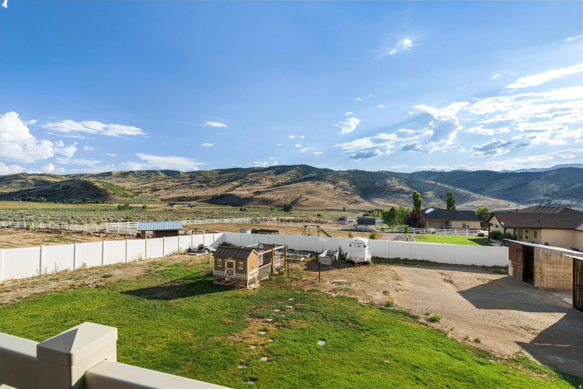 Expansive property featuring a vibrant green lawn area, a white perimeter fence, and a distant mountainous backdrop