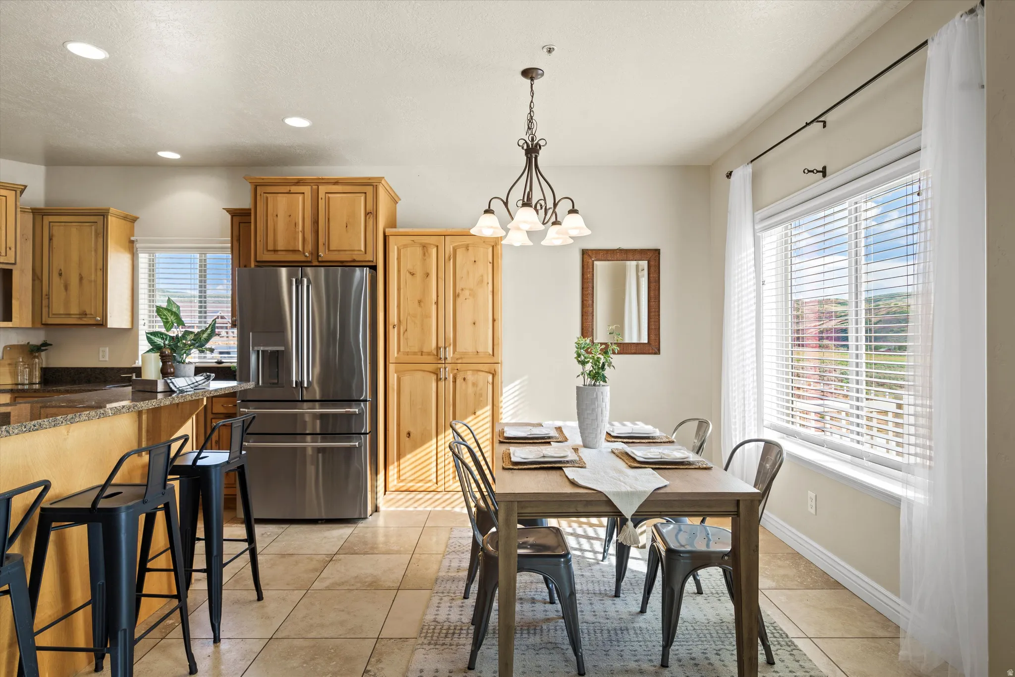 Kitchen and dining area featuring a breakfast bar with seating, stainless steel refrigerator, wood-finish cabinetry, and a large window with blinds