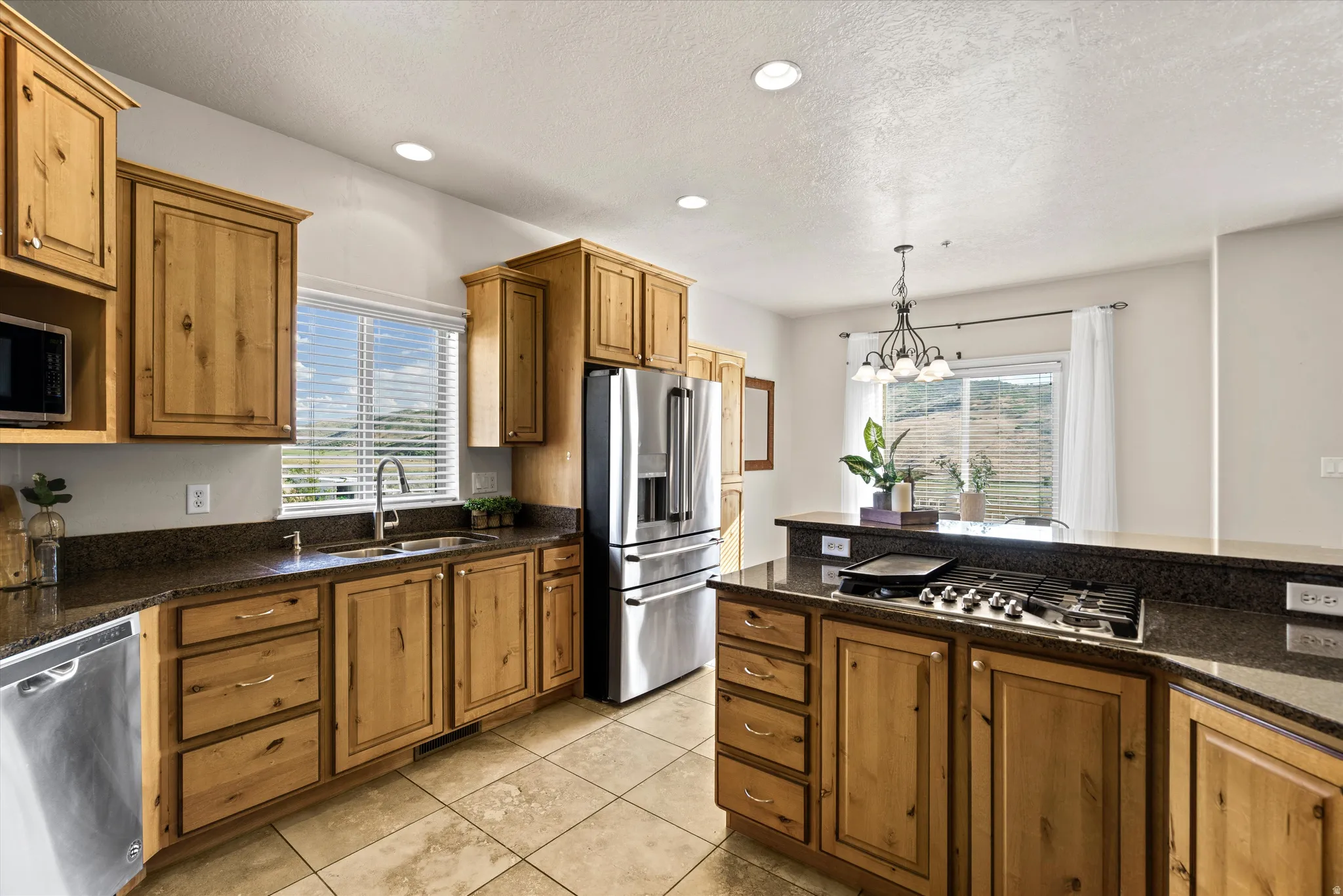 Kitchen featuring wood cabinetry, dark stone countertops, stainless steel appliances, and tile flooring