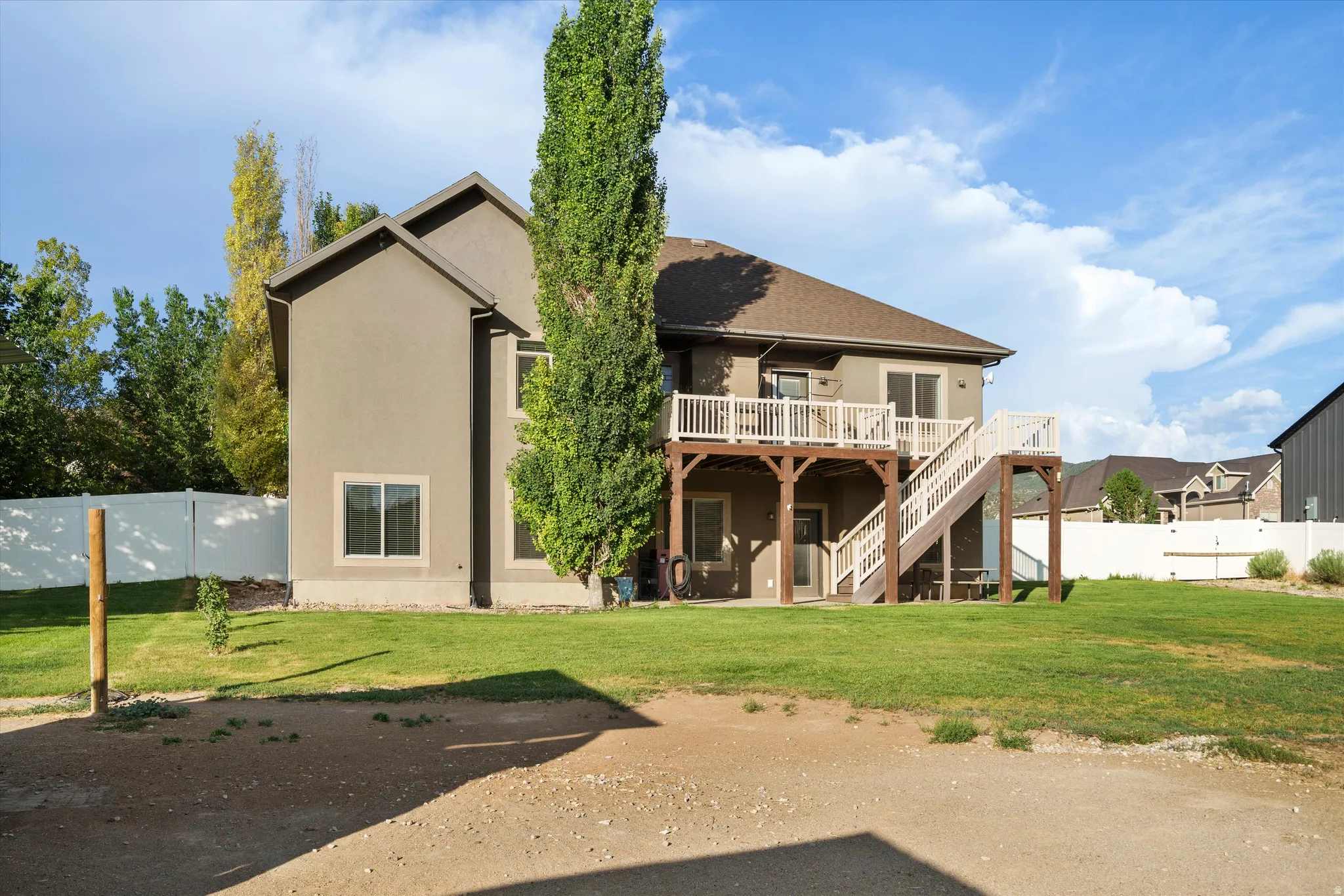 Rear exterior featuring a two-story stucco facade, an upper-level deck with white railings, and a walk-out lower level