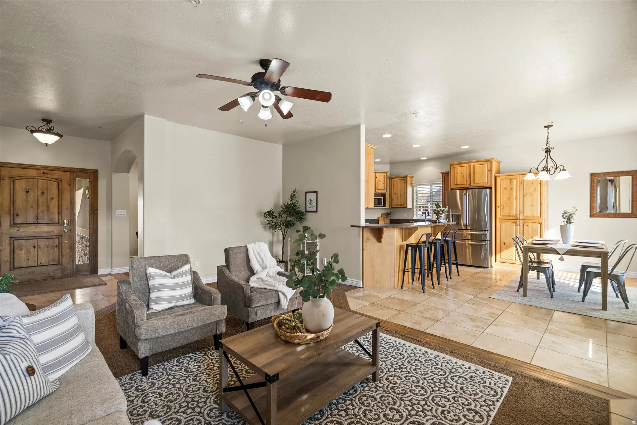 Open-concept living area featuring a wood-finish double entry door, an archway, a ceiling fan, and tile flooring throughout the kitchen and dining areas