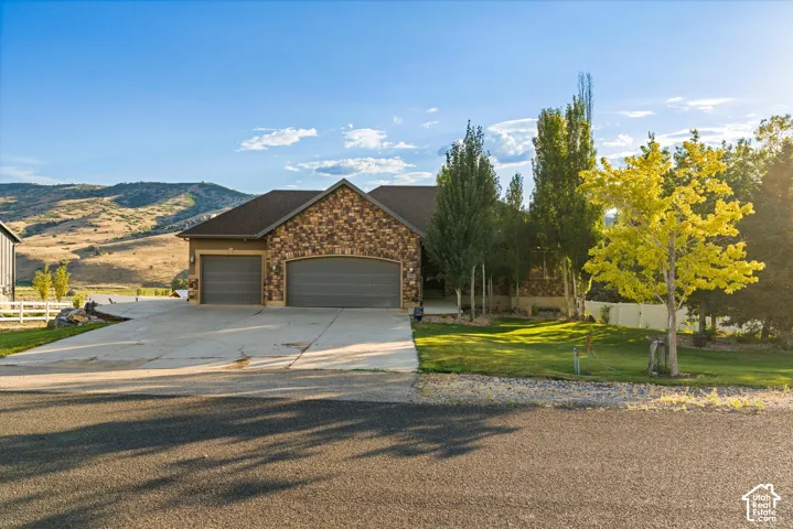 Stone and stucco exterior featuring a dark shingle roof, arched garage doors, and a concrete driveway