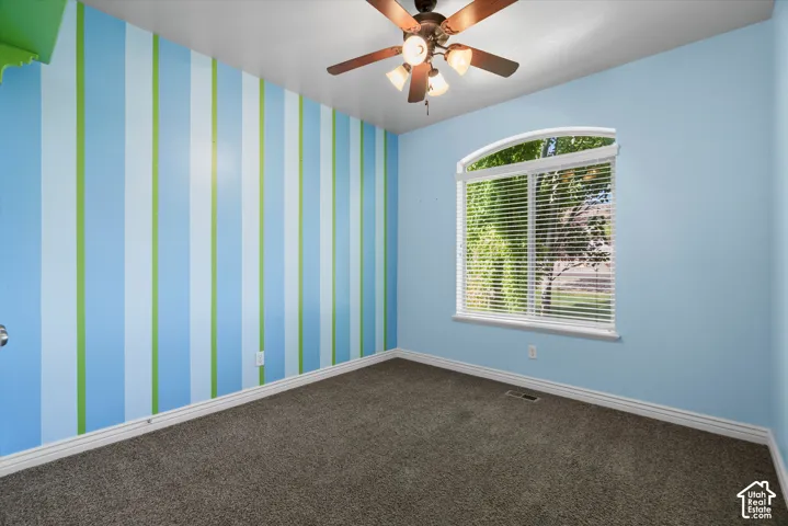 Carpeted room featuring a large arched window with horizontal blinds, a ceiling fan with integrated lighting, and a wall with blue and green vertical stripes