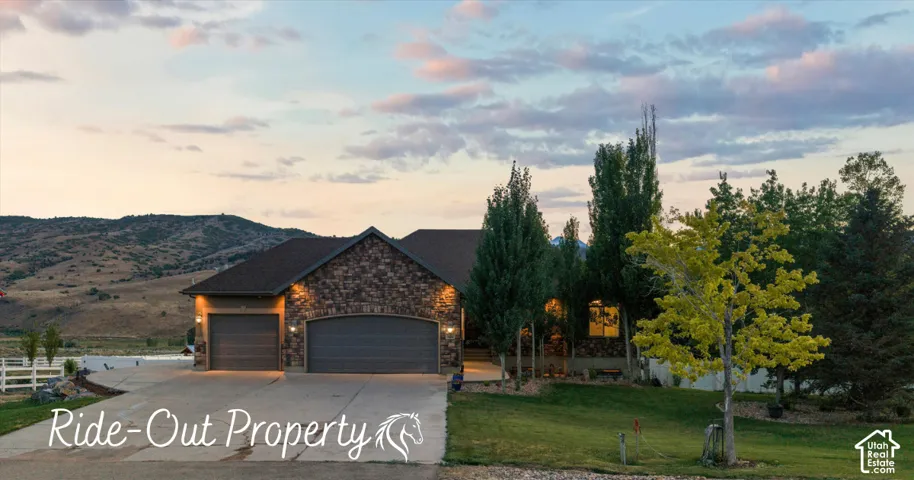 Single-story exterior featuring stone veneer siding, an attached three-car garage, concrete driveway, and expansive mountain backdrop