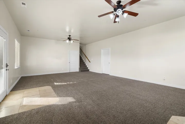 Spacious room featuring neutral carpeting, a tiled entry area, and two ceiling fans with integrated lighting
