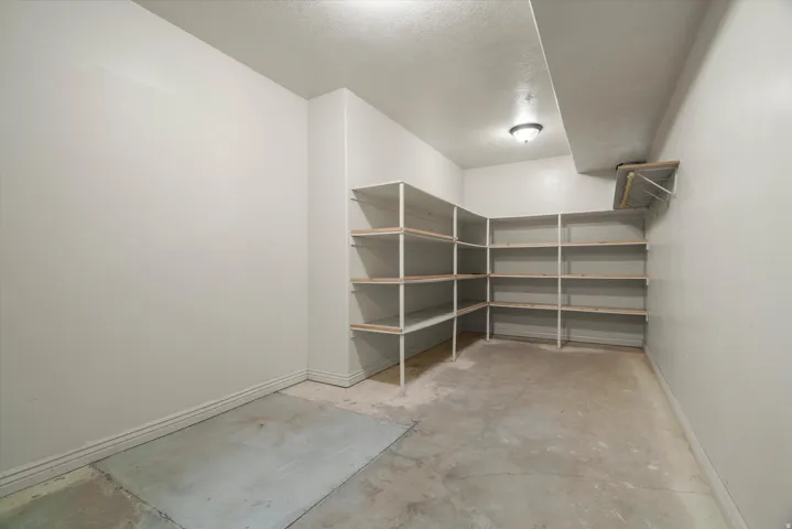 Spacious storage room featuring extensive built-in shelving, concrete flooring, and a ceiling-mounted light fixture