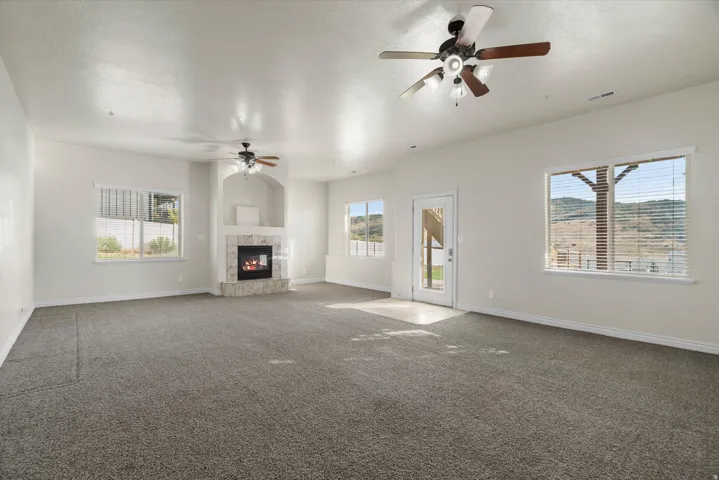 Spacious interior room featuring light-toned walls, textured gray carpeting, and multiple windows