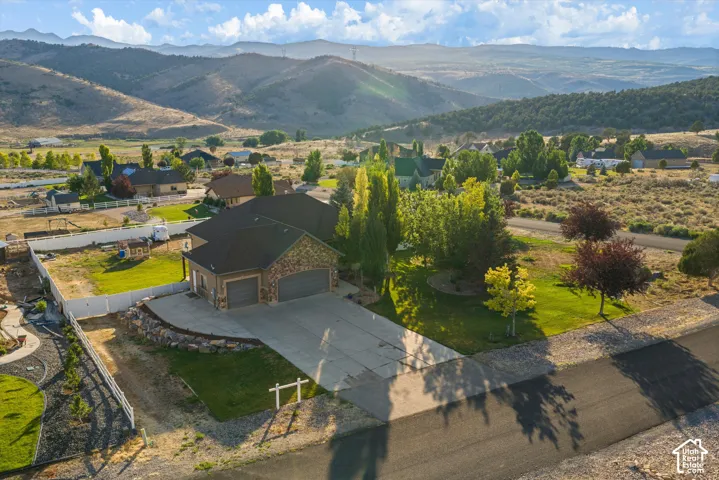 Stone and stucco exterior residence featuring a multi-car garage, concrete driveway, and landscaped front yard with mature trees
