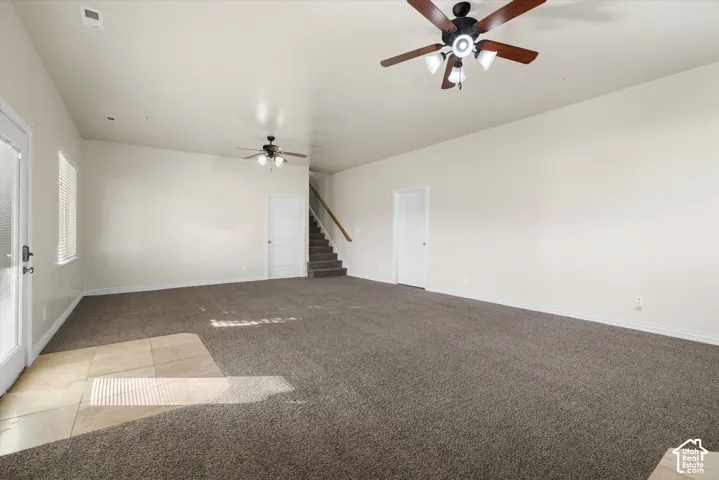 Spacious room featuring neutral carpeting, a tiled entry area, and two ceiling fans with integrated lighting
