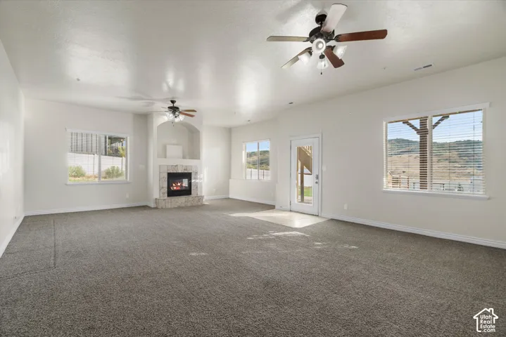 Spacious interior room featuring light-toned walls, textured gray carpeting, and multiple windows